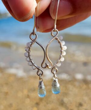 Handmade moonstone earrings with natural wire-wrapped aquamarine gemstones on sandy beach