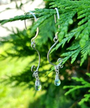 Handmade sterling silver aquamarine earrings dangling from an evergreen tree