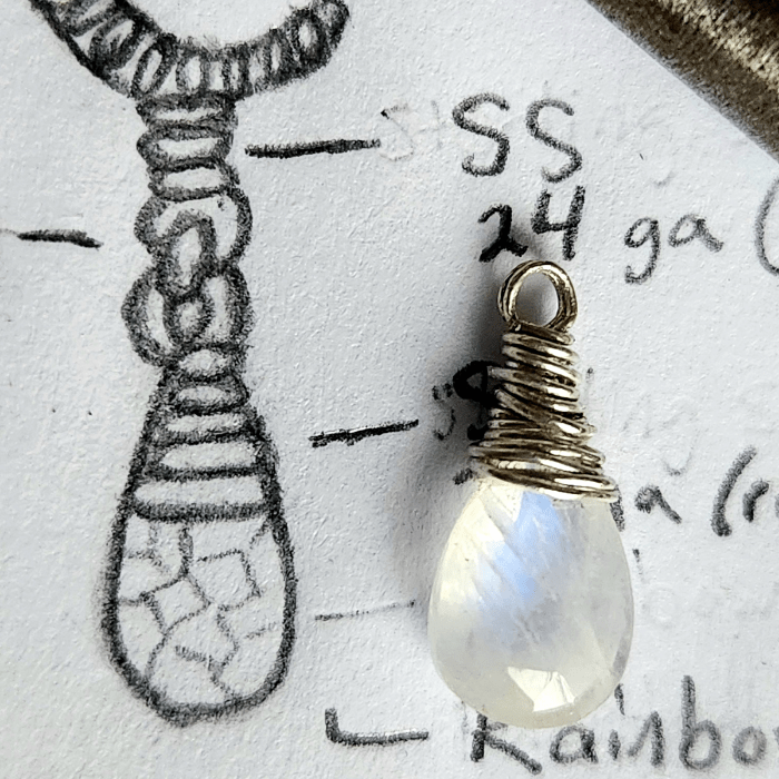 Closeup of wire-wrapped natural rainbow moonstone on night inspired jewelry design sketch