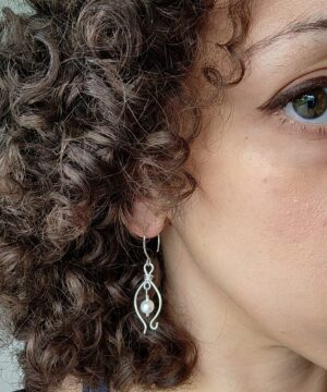 Wire-wrapped freshwater pearl earrings worn indoors