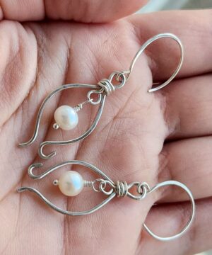 Wire-wrapped pearl earrings in sterling silver held in hands