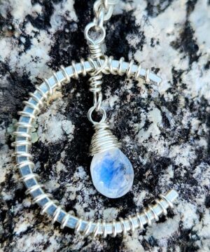 Close up of sterling silver wire-wrapped moonstone pendant on rock