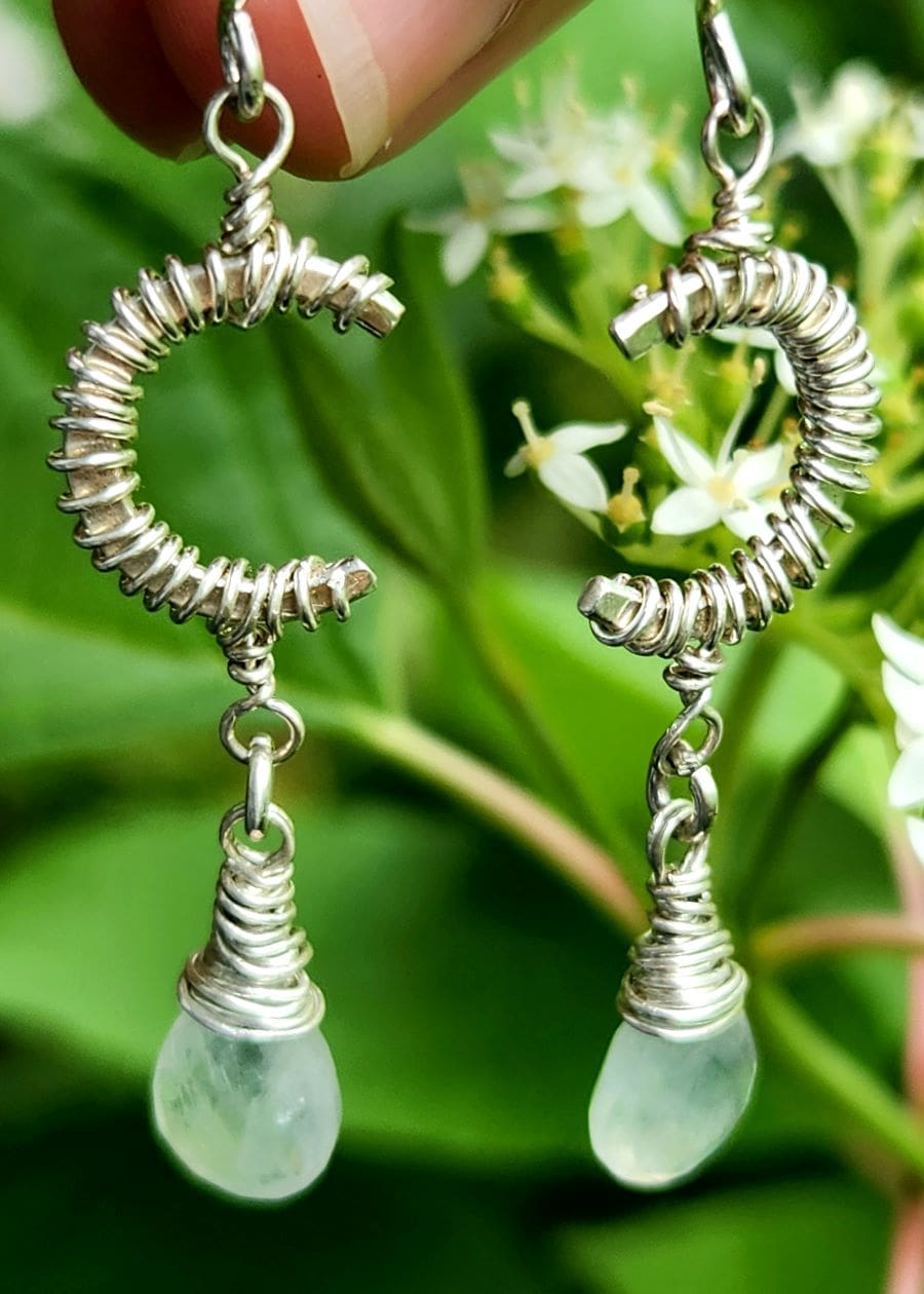 Handmade sterling silver crescent moon earrings dangling in nature with white flowers