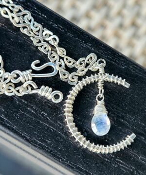 Handmade wire-wrapped sterling silver crescent moon pendant resting on chair