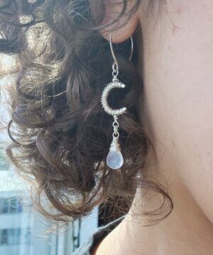 Wearing rainbow moonstone sterling silver crescent moon earrings indoor in front of window