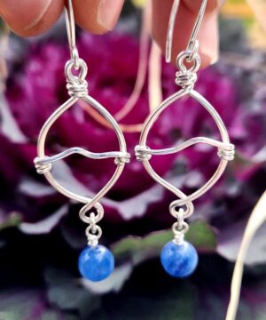 Handmade sterling silver kyanite drop earrings in front of flower