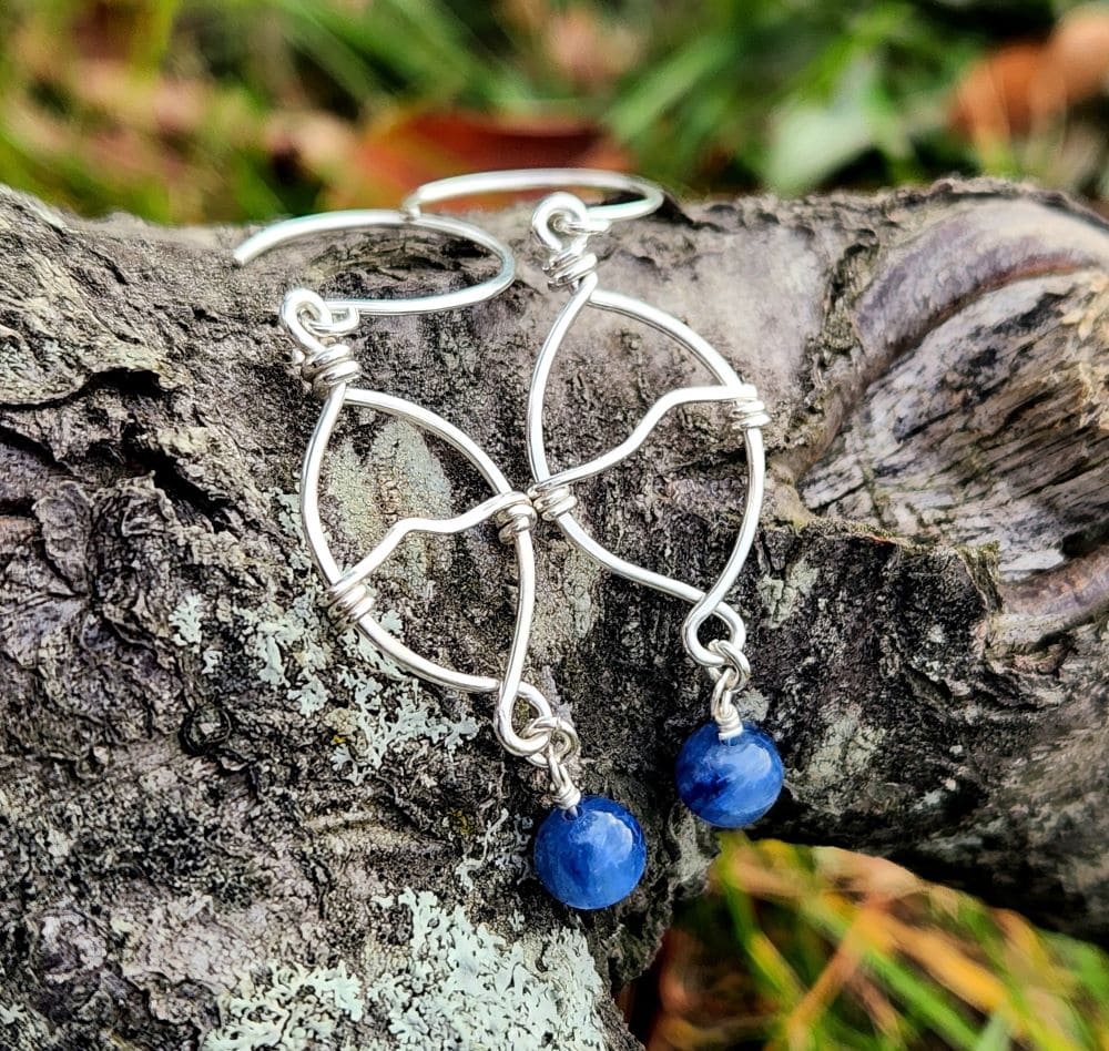 Handmade wire-wrapped kyanite earrings resting on rock, made with sterling silver
