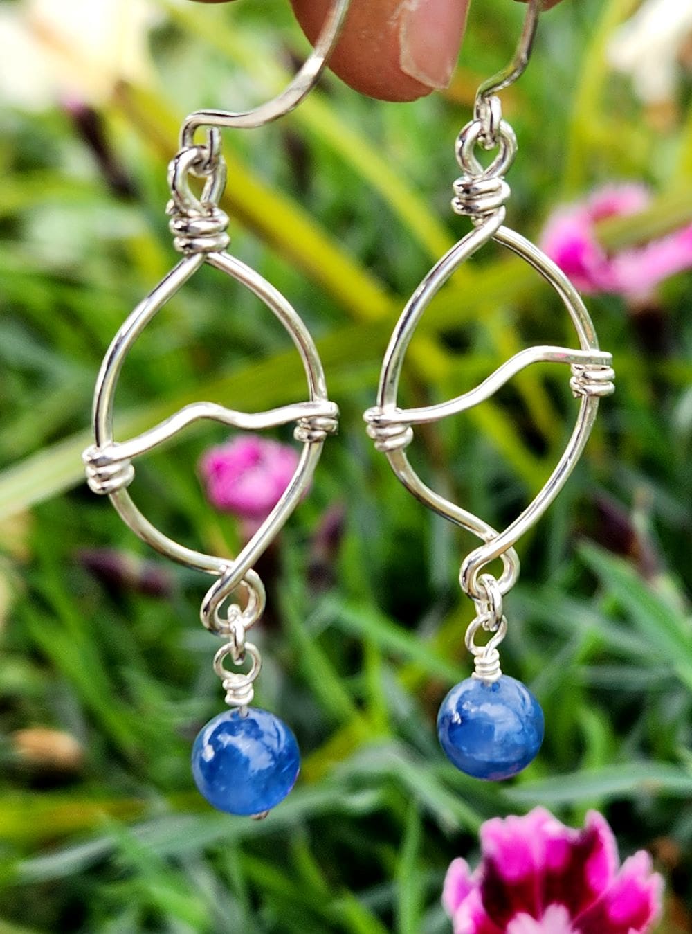 Natural kyanite dangle earrings in front of pink flowers