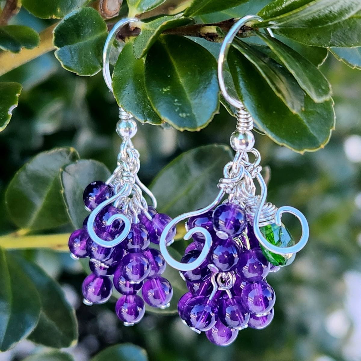 Handmade wire-wrapped grape cluster earrings hanging on a branch