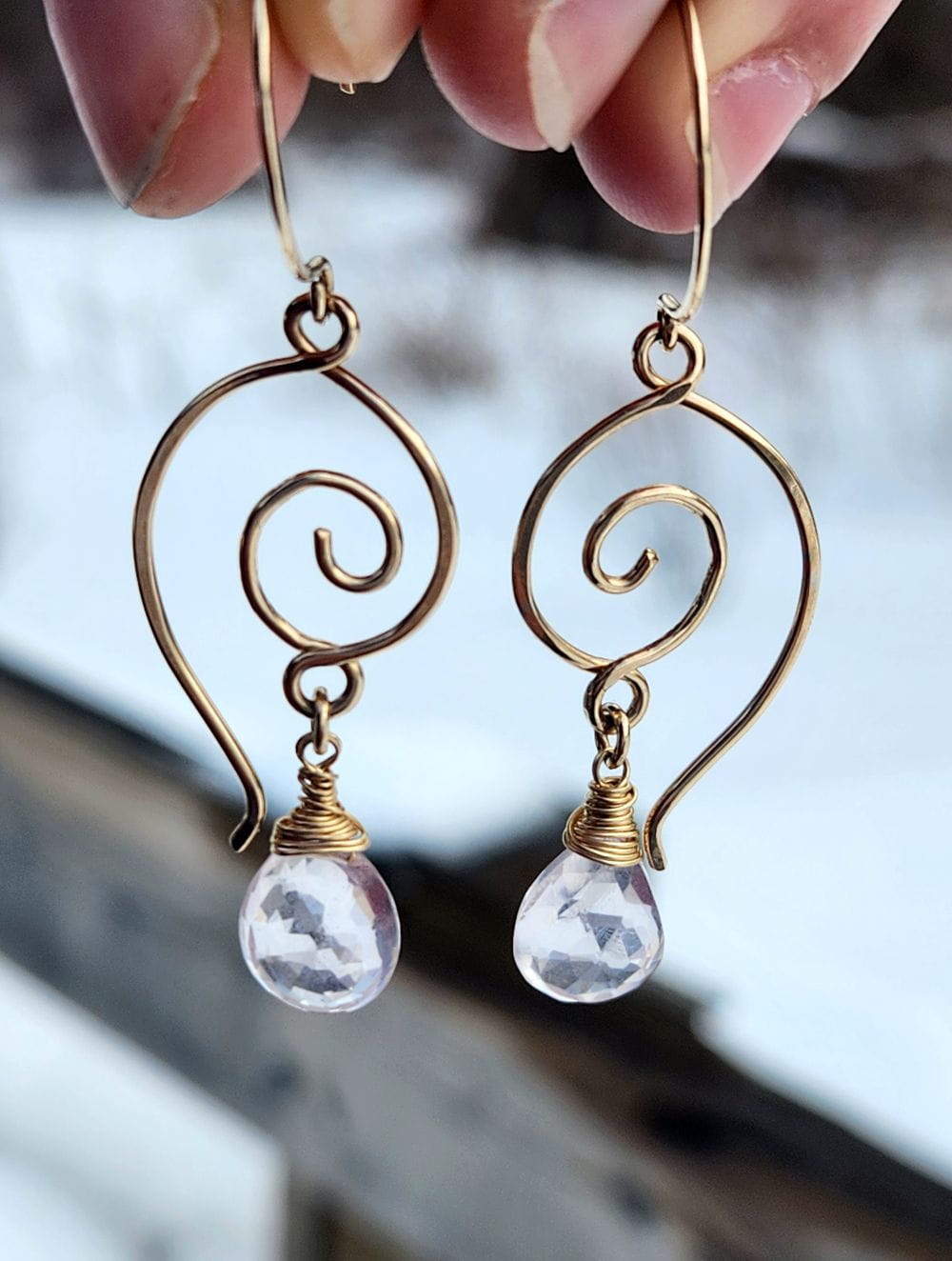 Handmade rose quartz dangle earrings in 14k gold-filled wire in front of snow