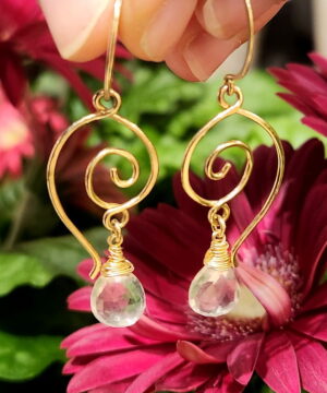 Handmade wire-wrapped rose quartz dangle earrings in front of flowers