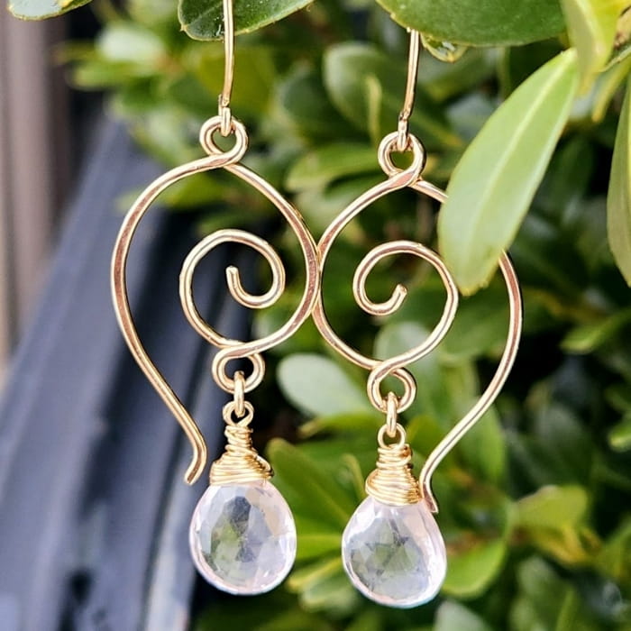Wire-wrapped 14k gold-filled heart earrings on a tree, dangling outside